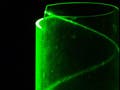A photograph of green laser light hitting the edge of a transparent cylinder and then curling into a helix due to total internal reflection.