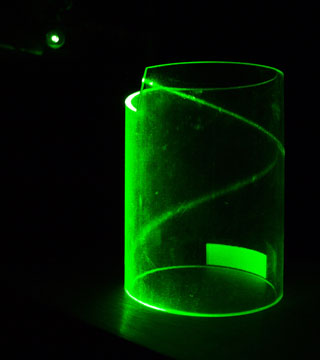 A photograph of green laser light hitting the edge of a transparent cylinder and then curling into a helix due to total internal reflection.
