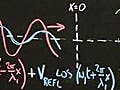 Professor standing in front chalkboard with diagrams and mathematics written on it.