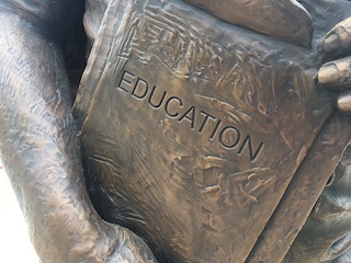 Photo of a metal statue holding a book that says "Education."