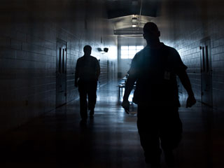 A dark hallway with two people walking toward the window with light