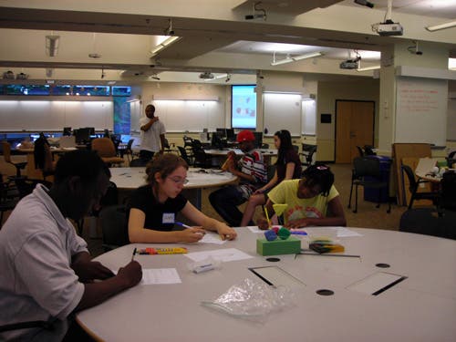 An image of three students working at a table using modeling clay. 