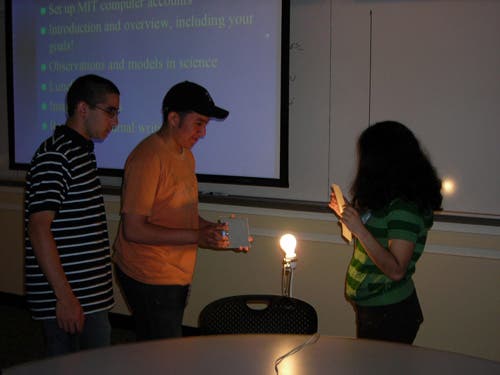 Photo of students in a dark room with a lit lightbulb. 