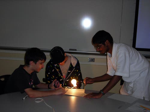 A photo of students working together to produce an image using the parts of a telescope. 