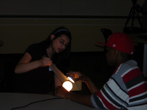 A photo of students working together to produce an image using the parts of a telescope. 