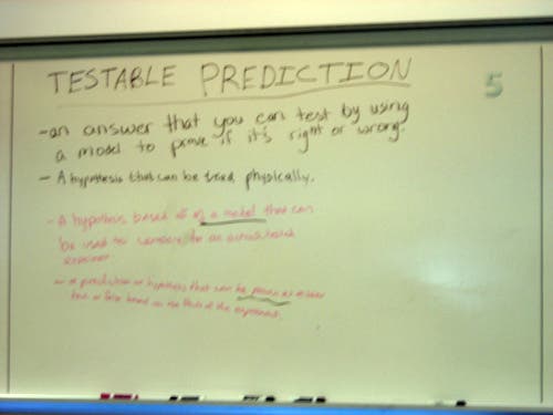 Handwritten notes on a whiteboard about testable predictions. 