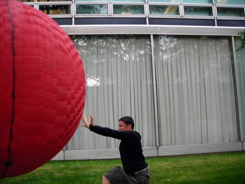 A trick photo showing a ball in the foreground and a person in the background so that it appears the ball is huge and about to run into the person. 