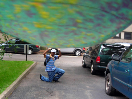 A trick photo in which a globe is in the foreground close to the camera and a person kneels on the ground in the background. It looks as if the person on the ground is holding up the world. 