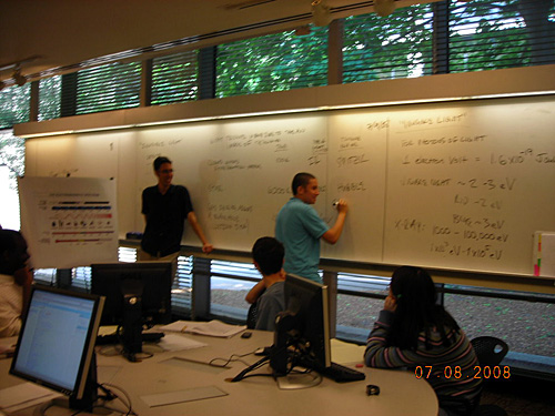 A teacher observes a student working on a problem involving invisible light at the whiteboard. 