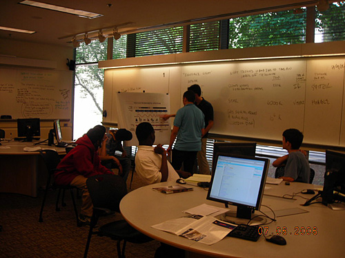 A photo of a teacher standing at the front of a classroom pointing at a chart explaining invisible light to students. 