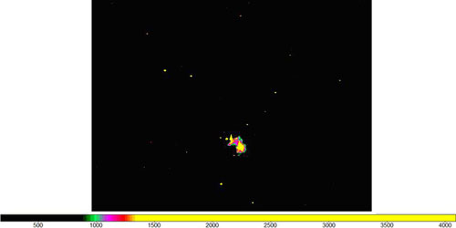 An image of a black sky with stars with a small burst of color in the middle. 