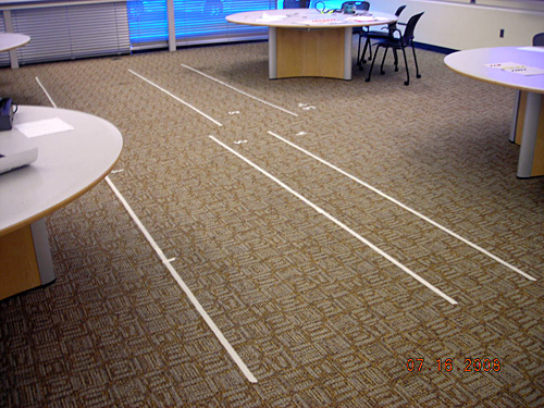 Six long pieces of white tape are laid down on the floor, and each one is labeled with a number. 