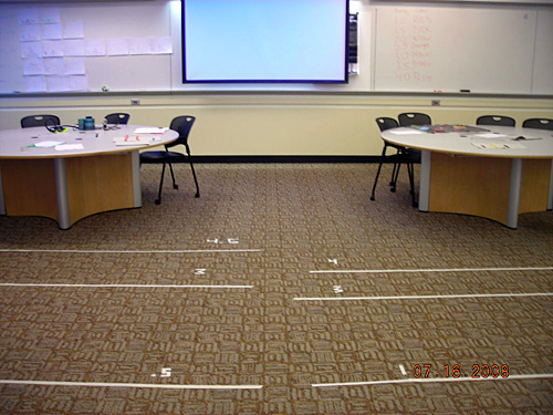 Six long pieces of white tape are on the floor labeled with the numbers.