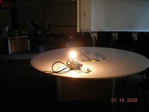 A photo of a demonstration of the brightness of a bulb. A very bright glowing lightbulb sits on a round table. 