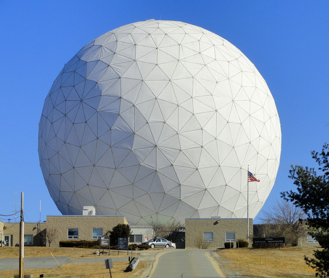 A huge white dome stands behind a small one story building. 