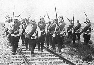 Photograph of a group of soldiers, rifles slung over their shoulders, marching along a railroad track.