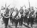 Photograph of a group of soldiers, rifles slung over their shoulders, marching along a railroad track.