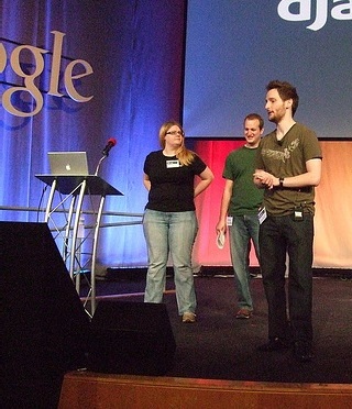 A photo of three people on a presentation stage at a conference.