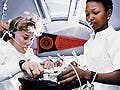 Two female astronauts work on an experiment onboard a space shuttle. 
