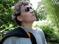 A photo of the profile of a man wearing sunglasses with trees in the background. 