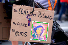 A sign made out of cardboard that says "The seas are rising and so are the moms." 