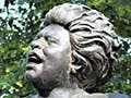 A bronze statue of a woman speaking into a microphone.