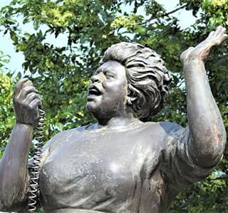 A bronze statue of a woman speaking into a microphone.